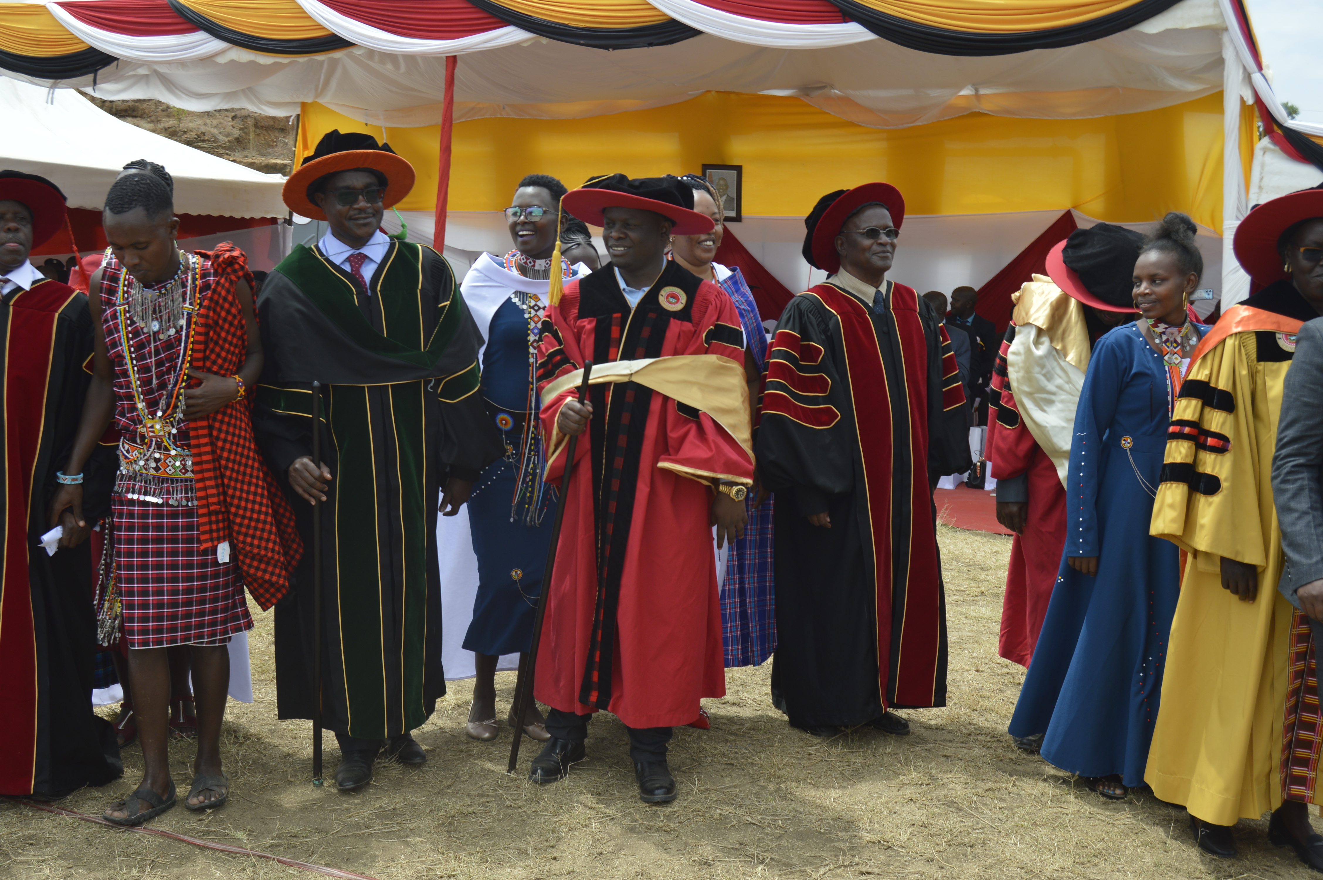 Education Cabinet Secretary Julius Migos Ogamba (in spectacles) and Narok County Deputy Governor Tamalinye Koech (in red gown) during the first graduation of the Maasai Mara Technical Voluntary Education and Training (TVET) join Maasai dancers for a jig