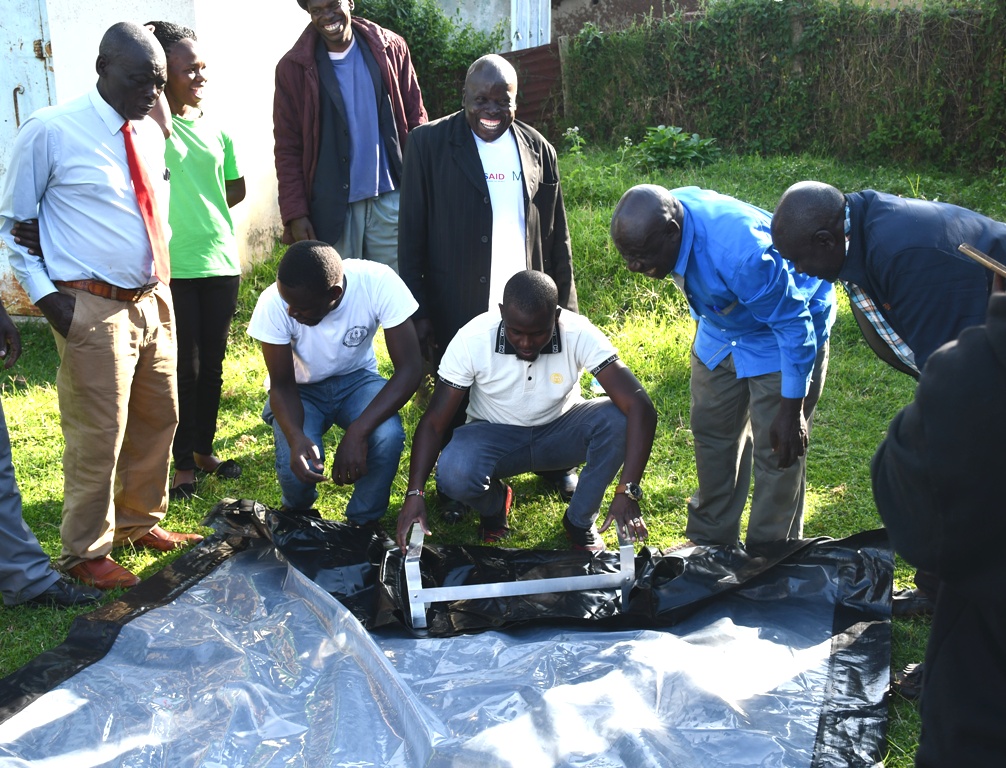 odgers Alinda from Sky Bold (white T-shirt) shows beneficiary CBO representatives how to fix a bubble-dryer at the Agriculture offices in Lumakanda