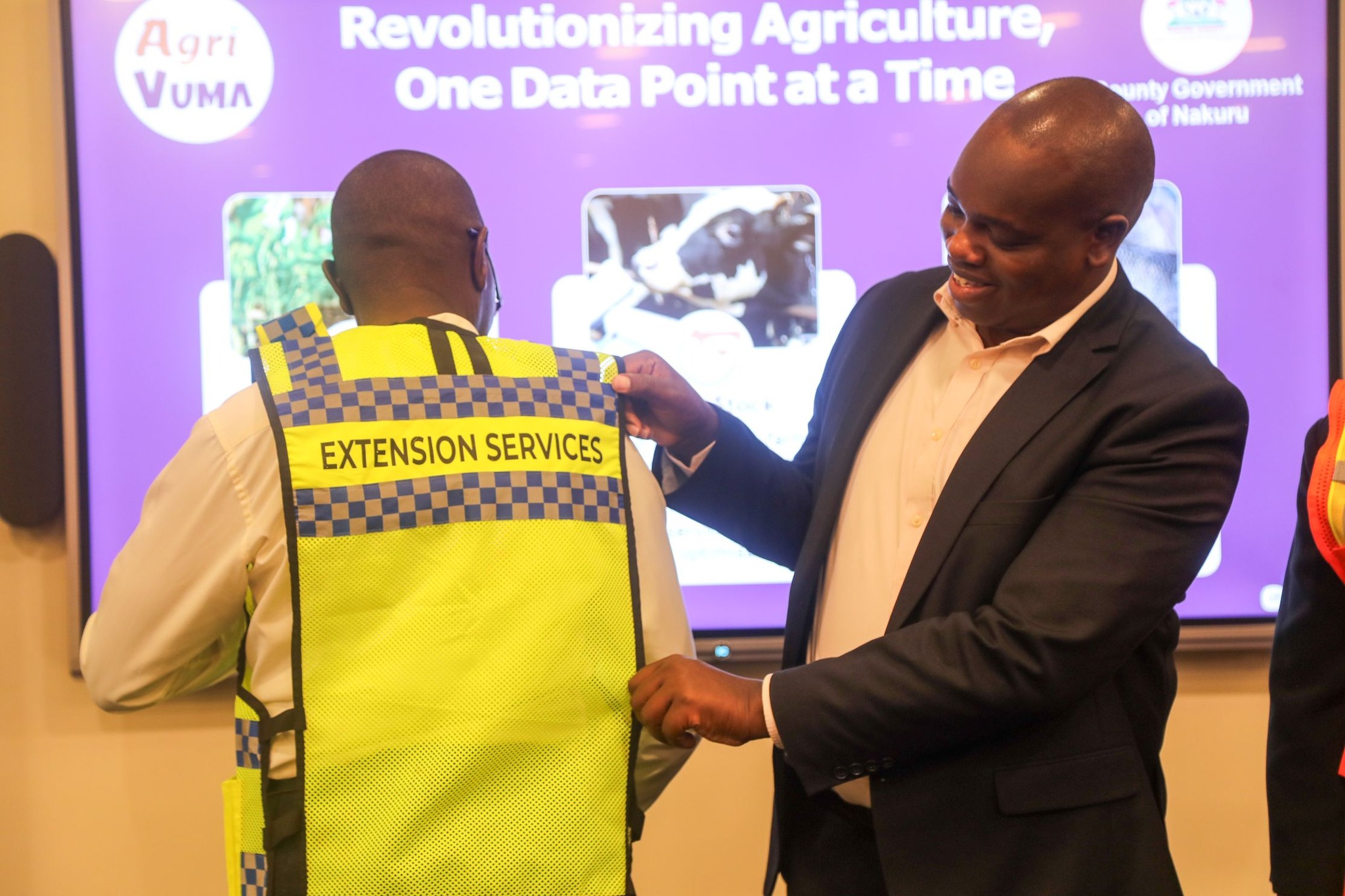 Chief Officer Newton Mwaura (agriculture) assisting an extension officer to wear an identification jacket