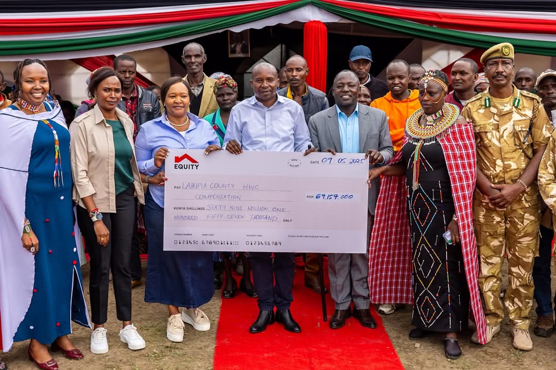 Deputy President Prof. Kithure Kindiki (centre in white shirt) accompanied by CS Tourism and Wildlife Rebecca Miano (L), and Laikipia Governor Joshua Irungu display a dummy cheque for victims of human-wildlife compensation at Naibor centre