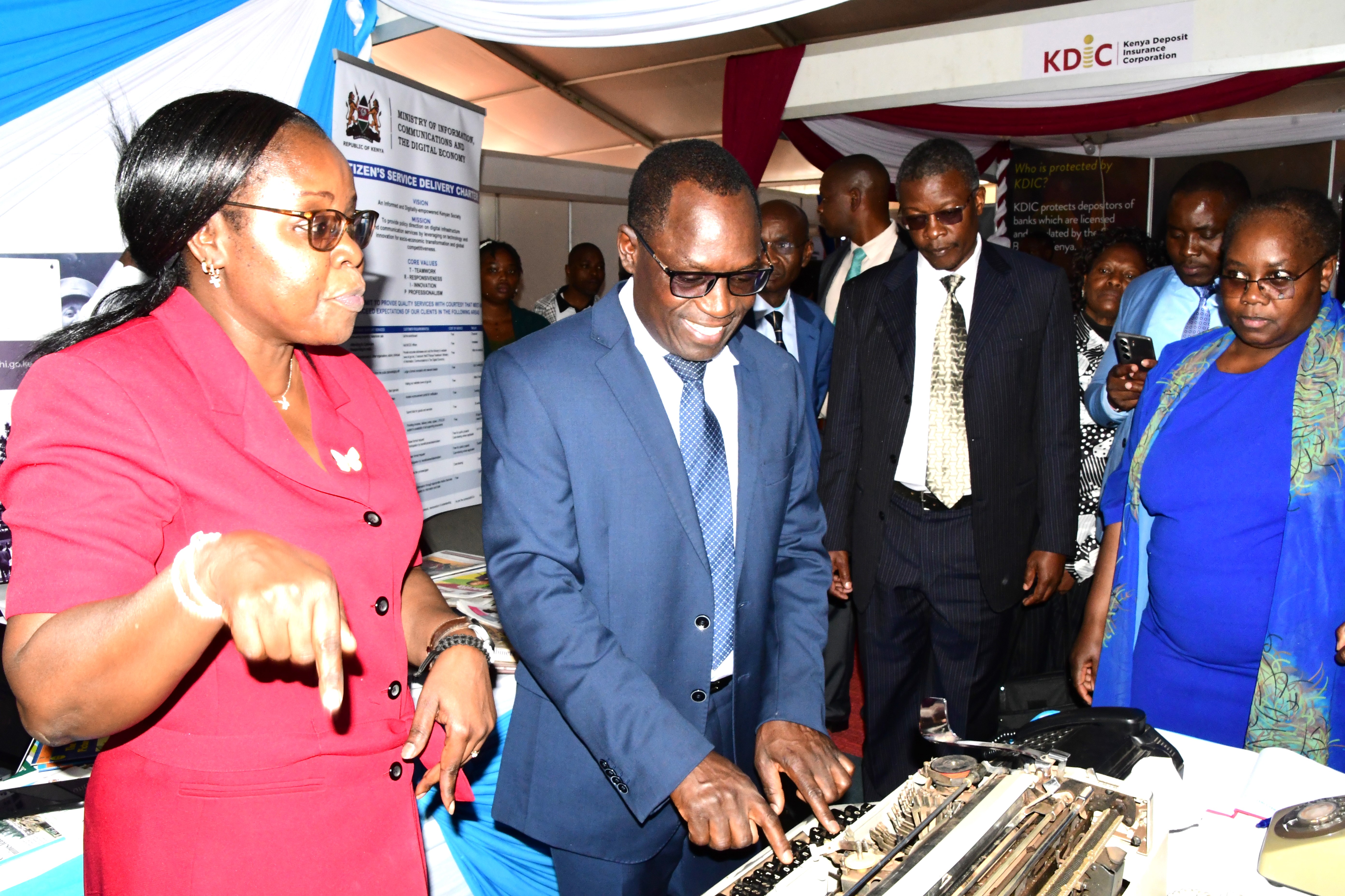 Principal Secretary, State Department for Broadcasting and Telecommunication Stephen Isaboke (2nd left) is being briefed by Officers Rosemary Ngesa (left) Odhiambo Omondi (third left) and Rose Andanje (second right) on the evolution of KNA Tools of Trade at the ICT Ministry’s stand during the 2025 African Public Service Day (APSD) National celebrations at Kenyatta International Convention Center (KICC) Nairobi. PHOTO/NORAH BOCHERE