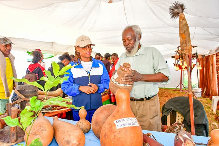 County Executive Committee Member for Trade, Cooperatives, Culture and Tourism, Diana Kendi (left) is taken through a demonstration of the names and functions of the Gikuyu tools by Mathenge Iregi