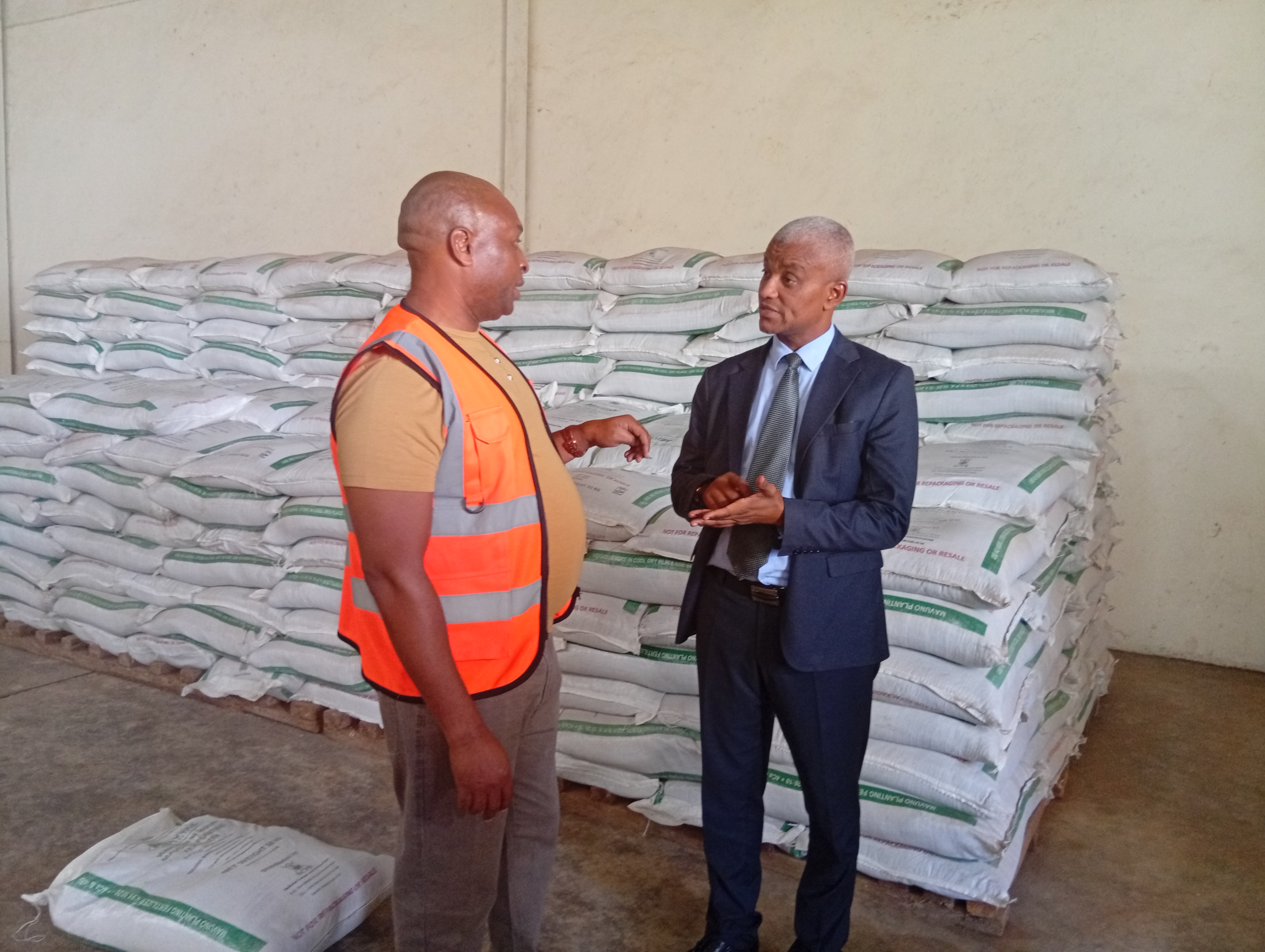 The National Fertilizer Technical Committee Chairman Haron Khator (left) presents a Thika farmer with subsidized fertilizer she had purchased at the National Cereals and Produce Board in Thika town .